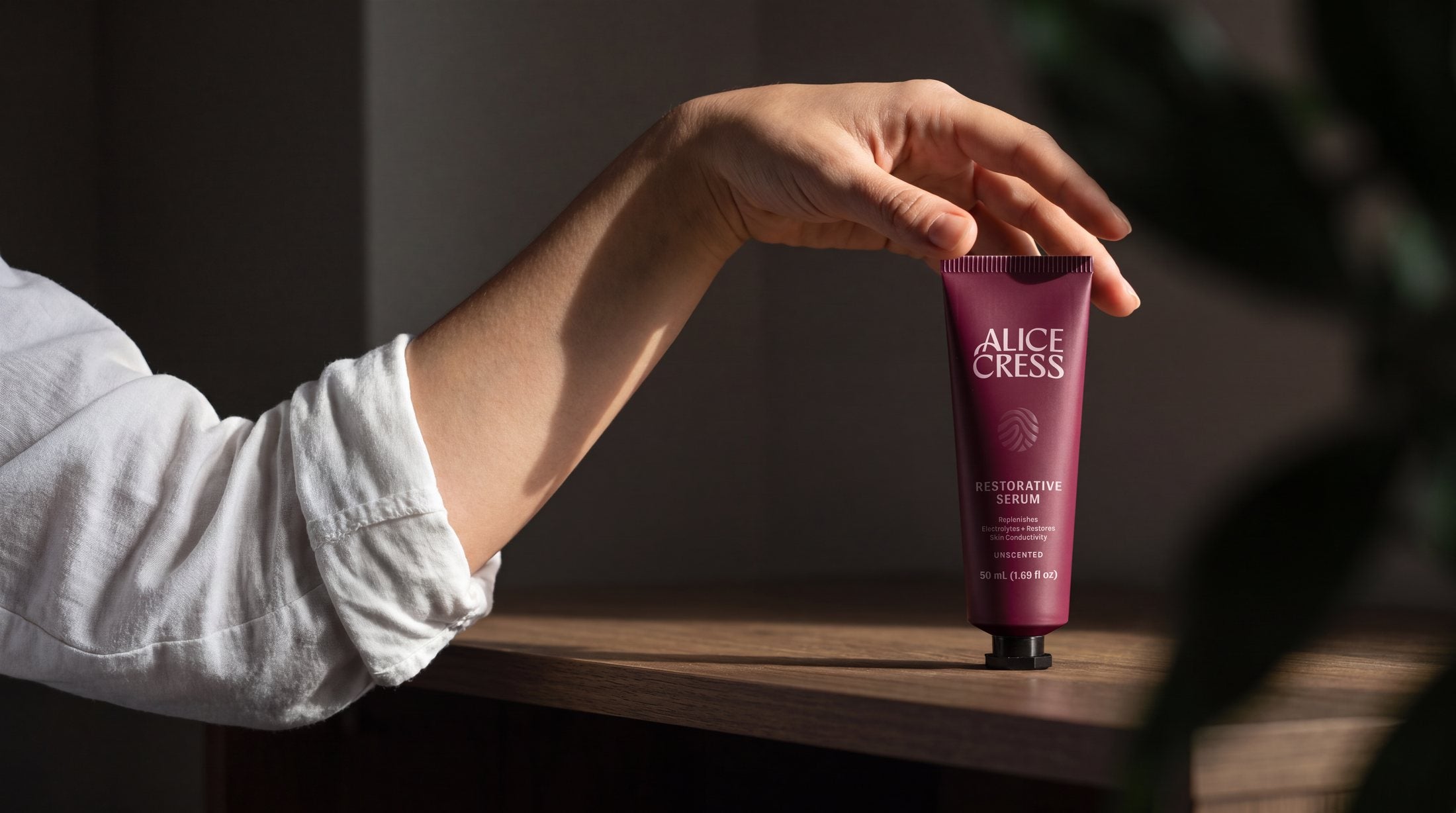 A hand holding a 50 ml tube of Alice Cress Restorative Serum on a wooden shelf