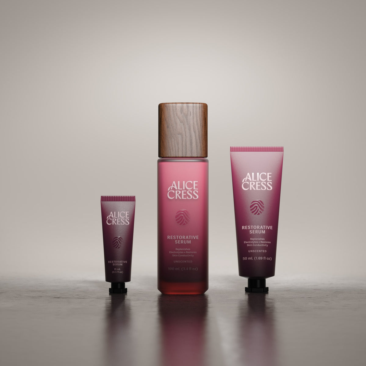 Three Alice Cress skincare bottles and tubes in a burgundy color scheme, arranged on a reflective dark surface against a neutral gray background.